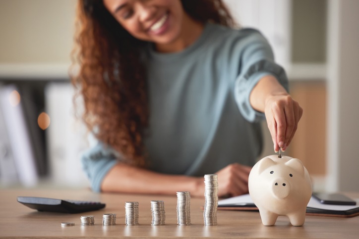 young-african-american-woman-money-putting-coins-into-a-piggybank-at-home-mixed-race-person-counting-coins-while-financial-planning-in-her-living-room-saving-investing-and-thinking-about-the-future